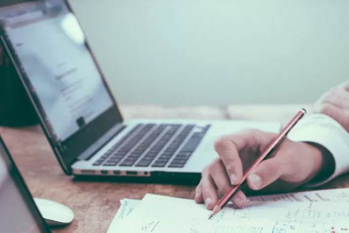 someone holding a pencil with laptops on the desk